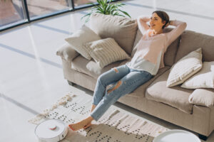 woman relaxing sofa while robot vacuum cleaner doing housework